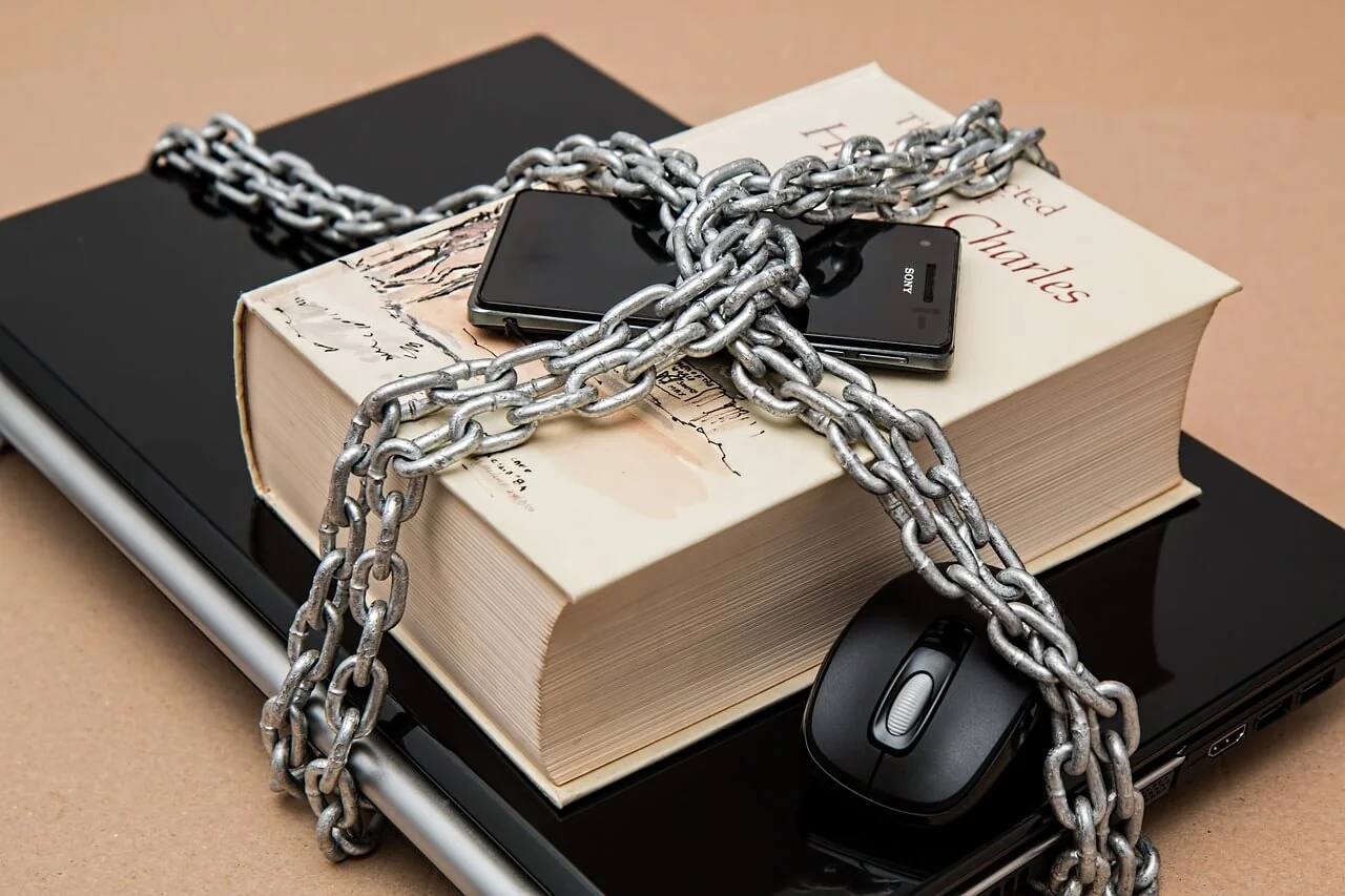 Libro, ordenador portátil, teléfono y mouse de ordenador asegurados con una cadena.