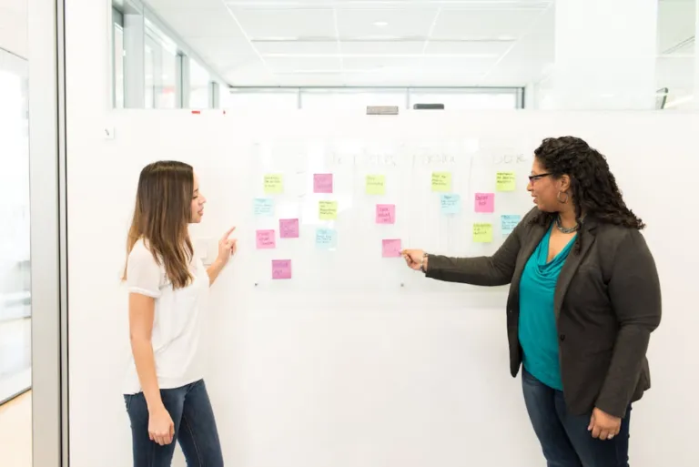 Two women talking in front of a board.
