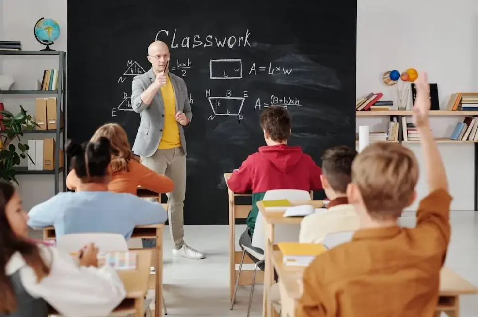 Profesor en clase delante de la pizarra haciendo preguntas a los alumnos.