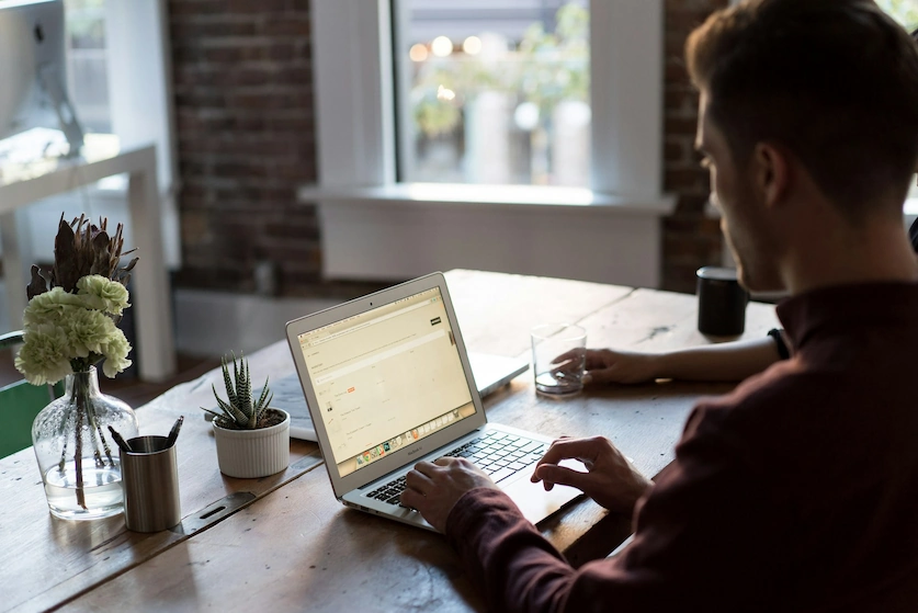 A guy working on a laptop placed on top of a wooden table.