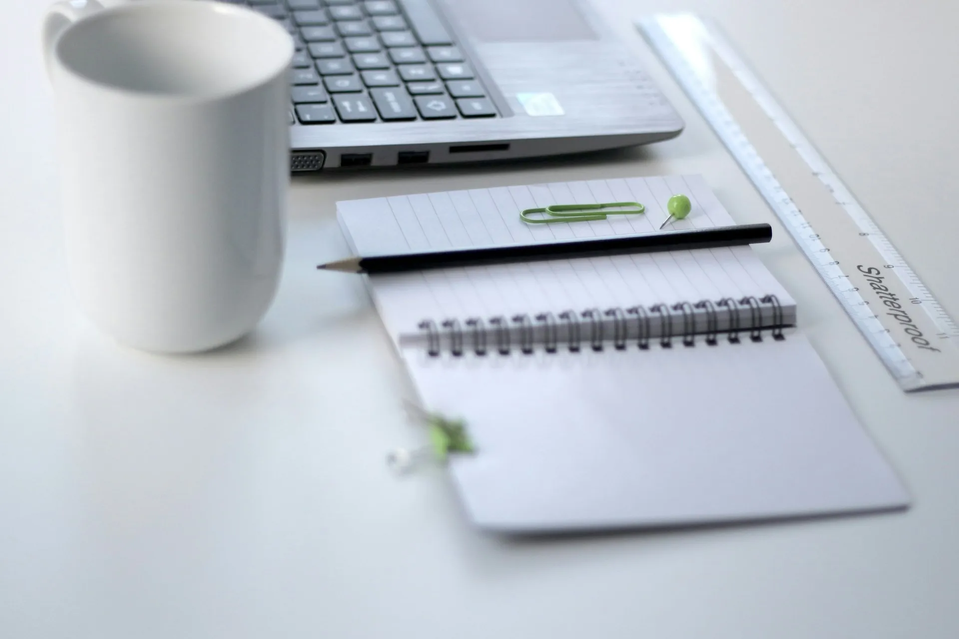Um notebook, caderno, lápis, régua, notebook e xícara de porcelana branca em uma mesa. Controle de tempo para educadores