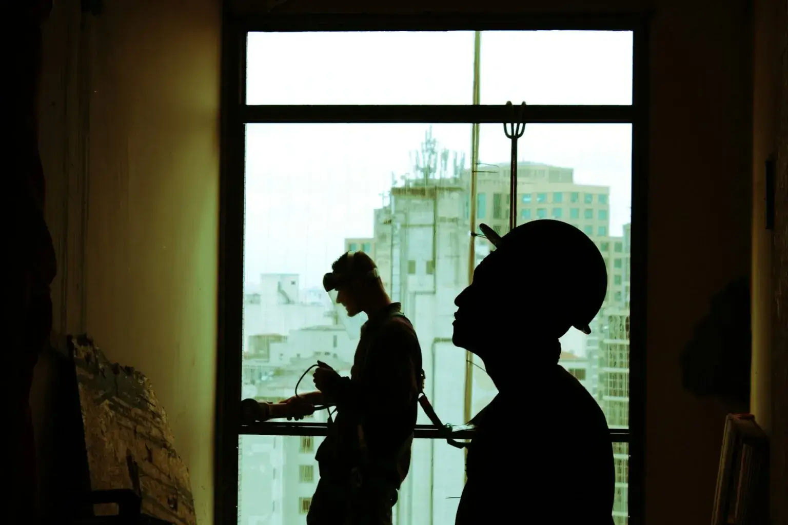 Dos obreros trabajando en la obra, fotografiados a contraluz desde una ventana.