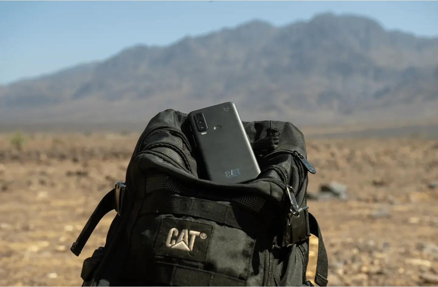 Teléfono resistente Cat S75 colocado sobre una mochila negra en un paisaje desértico.