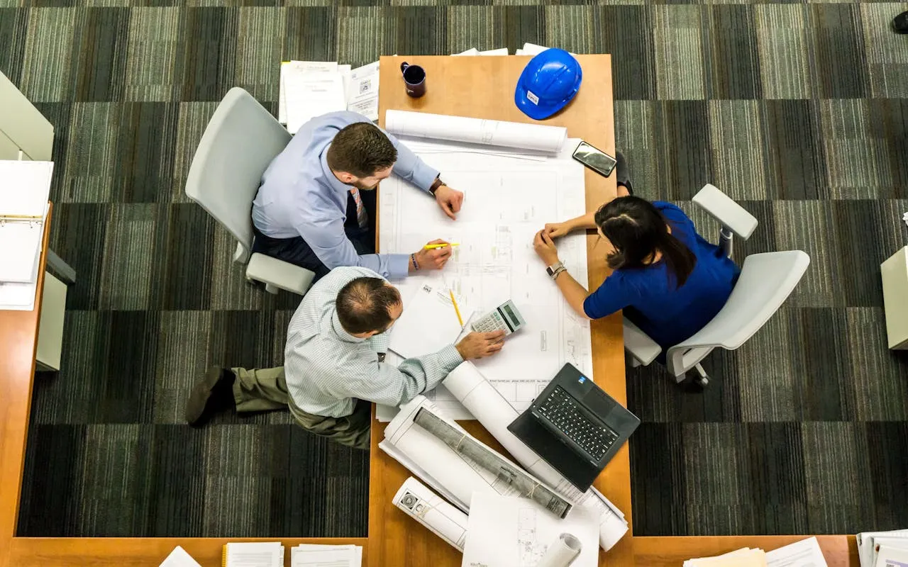 Réunion entre des employés du secteur de la construction, discutant d'un plan de projet présenté sur une table. 