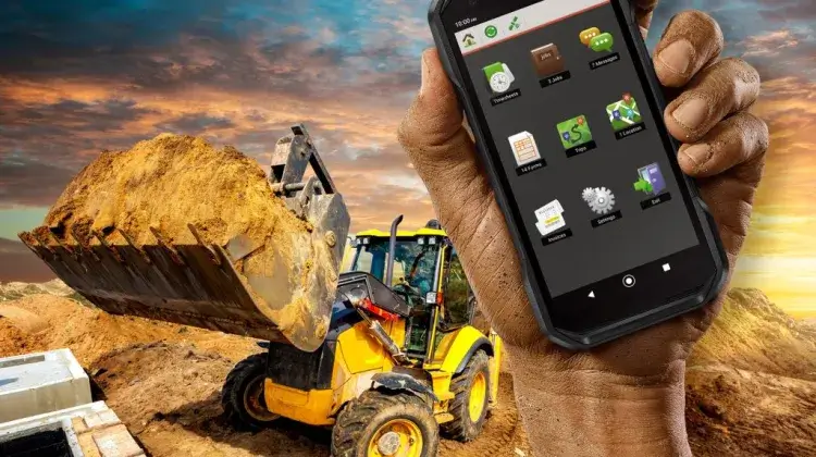 Teléfono resistente Kyocera DuraForce PRO 3 sostenido en una obra con una pala cargadora al fondo.