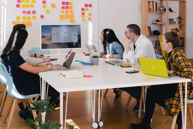 Un grupo de empleados reunidos, mirando una presentación en la pantalla del ordenador mientras están en la oficina.