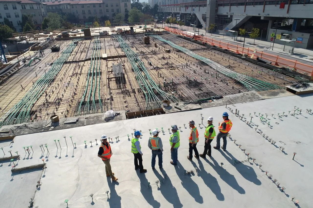 A team of engineers and construction workers in safety gear inspecting a large construction site with reinforced concrete and exposed rebar.