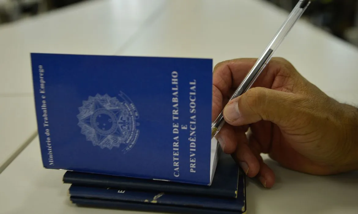 Empregador escrevendo na carteira de trabalho de seu funcionário, abrangido pela CLT