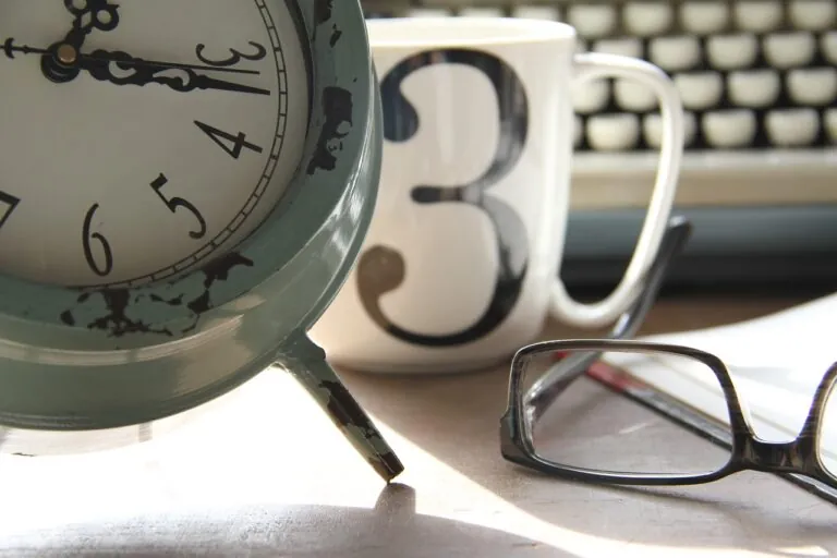 Cup, keyboard, clock and glasses displaying work hours