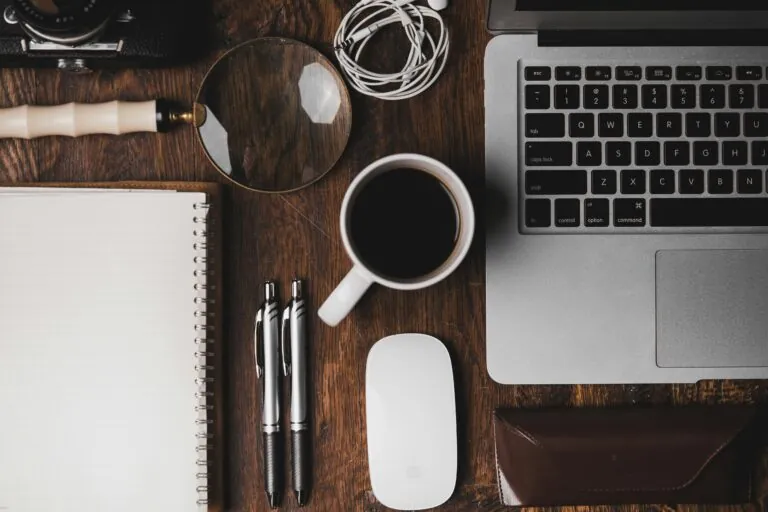 Desk with laptop, cffee cup, pens, and notepad