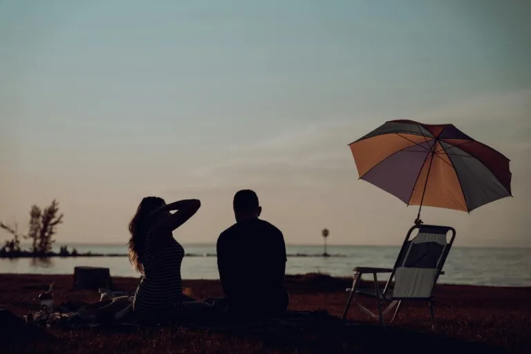 Coppia con ombrellone e sdraio in spiaggia durante il tramonto.